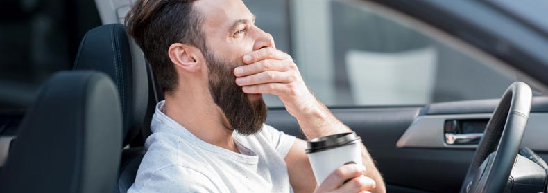 man yawning with coffee in hand