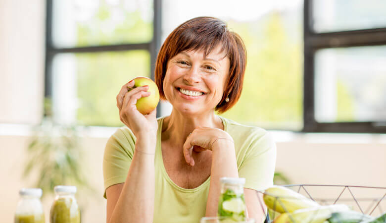 woman with short brown hair, wearing green shirt and holding up apple