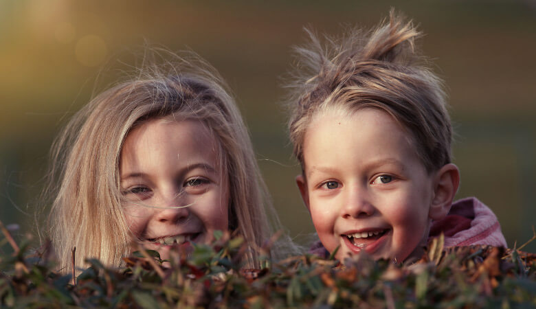 Closeup of a young brother and sister smiling behind a hedge after they've overcome their dental anxiety