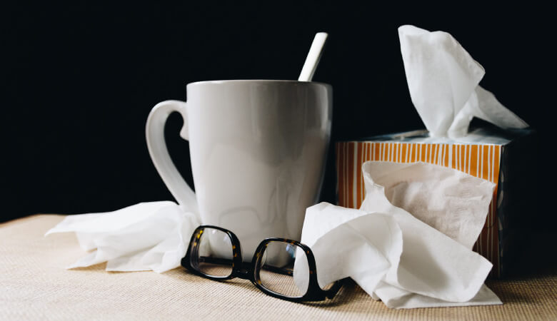 A box of tissues next to used tissues and a white mug when someone has the common cold