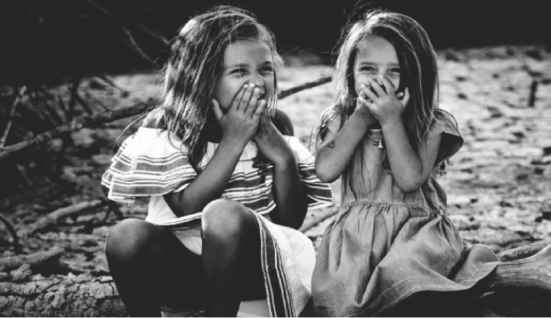 two young girls hold their mouths while laughing