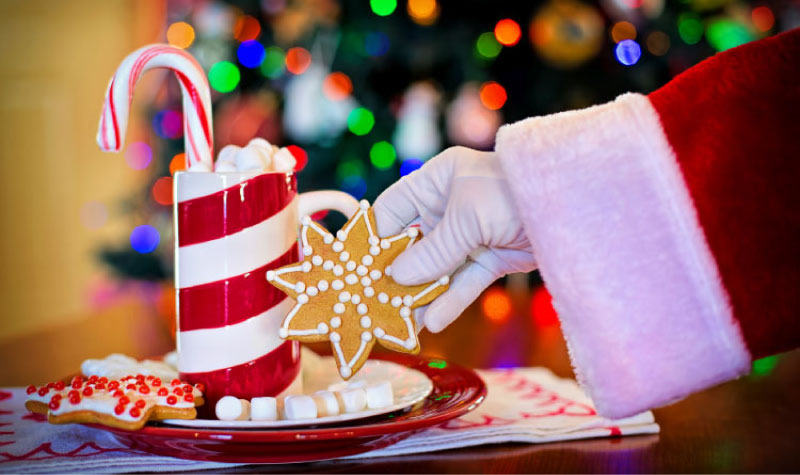 santa's gloved hand reaching for candy cane and cookies which can cause tooth decay