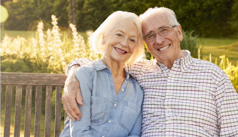 senior couple sitting on a bench smiling after learning how to clean their dentures