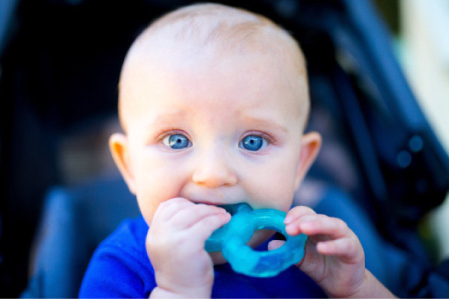blue eyed baby boy chewing on a plastic rattle